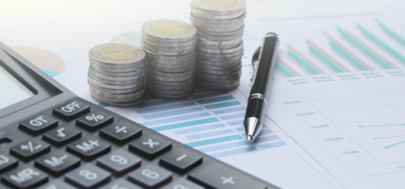 Calculadora, pilhas de moedas e uma caneta sobre gráficos financeiros